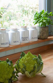 Romanesco cauliflowers on wooden worksurface in front of storage jars and potted basil plant on kitchen windowsill