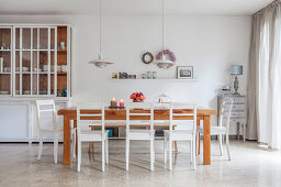 White dresser with glass doors and wooden table with white chairs in dining area