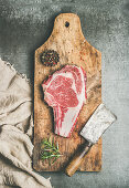 Flat-lay of raw prime beef meat dry-aged steak rib-eye on bone with seasoning and chopper knife