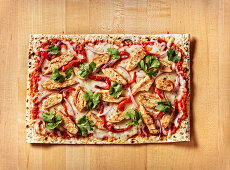 BBQ Chicken Flatbread Pizza on butcher block table with cilantro, roasted red peppers and mozzarella white cheese