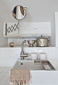 Waschbecken, silberne Töpfe und Kosmetikspiegel im Badezimmer mit weißen Wandfliesen