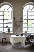Tisch mit weißem Tuch vor einer Wand mit großen Bogenfenstern