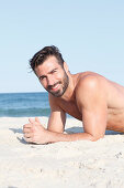 A young topless man lying in the sand