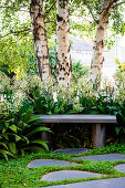 Stone slabs in front of a stone bench under three birch trees