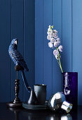 Dekovogel, Geschirr und Glasvase mit Blume vor blauer Wand