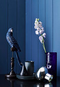 Decorative bird, crockery and glass vase with flower against blue wall