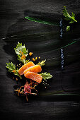 Food art: salmon with caviar, celery, roasted onions and sesame seeds on a black painted surface