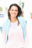 A brunette woman wearing a light t-shirt and a pink jumper with a blue jumper over her shoulders