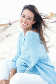 A brunette woman wearing an oversized blue jumper and white trousers