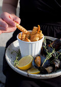 A woman holding a plate of french fries and mussels in a thyme, lemon, white wine and garlic sauce