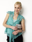 Blonde Frau in türkisfarbener Bluse, mit Zeitung unter der Arm