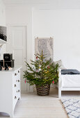 Decorated Christmas tree and white chest of drawers in white room