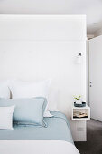 Doppelbett mit weißer und hellblauer Bettwäsche vor Raumteilerwand im Schlafzimmer