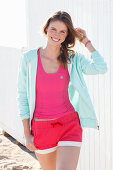 A young woman on a beach wearing a pink top, a jacket and shorts