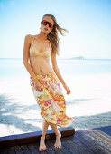 Junge Frau im Bikiniorberteil und Rock mit Blumenmuster am Strand