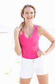A blonde woman on a beach wearing a pink top and light shorts