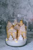 Gingerbread city in a glass jar with lights on a gray background
