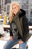 A blonde woman wearing a top decorated with a sequinned skull, a winter jacket and jeans