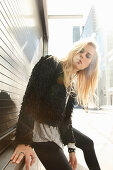 Junge blonde Frau in Tunikabluse und schwarzer Kunstfelljacke
