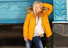A young blonde woman wearing a yellow quilted jacket and jeans
