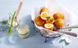 Breaded eggs in parchment paper in a metal basket next to a mustard dip and remoulade