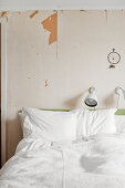 Weiße Bettwäsche auf Doppelbett, darüber Leselampe und Traumfänger an Wand mit abgeblätterter Tapete