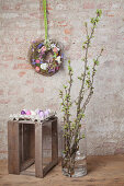 Frühlingszweige in der Bodenvase vor der Wand mit Blumenkranz