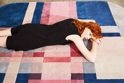 Rothaarige Frau in schwarzem Kleid liegt auf dem Teppich