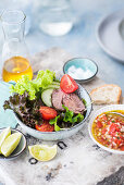 A mixed leaf salad with beef fillet, cherry tomatoes, tomato chutney and limes