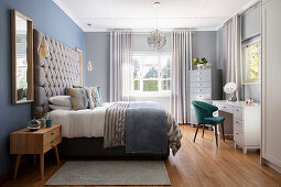 Schlafzimmer in hellen Grau- Blautönen mit Doppelbett, grossem gepolstertem Kopfteil und Schminktisch