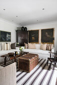 Sofas with linen covers, vintage coffee table, steamer trunk on striped rug and paintings on wall