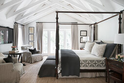 Himmelbett, Hussensessel und runder Tisch im Landhaus-Schlafzimmer mit Dachkonstruktion aus Holz