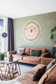 Brown leather sofas and wall hanging with animal skull in living room with green wall