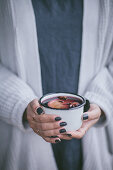 Frau hält einen Becher Tee oder Glühwein mit Sternanis und Orangenscheibe