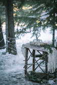 Macrame runner and gifts on small wooden table in snowy woods