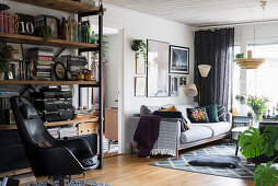 Black leather armchair in front of shelving in living room with pale sofa in background