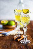 Traditional italian lemon alcohol drink limoncello with pieces of lemon and rosemary herb on dark wooden table