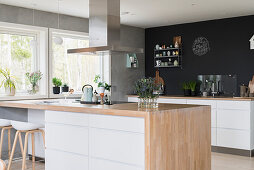 Island counter with pale wooden worksurface and kitchen counter against black wall in open-plan kitchen