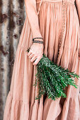 Woman in nostalgic dress holds a bunch of rosemary sprigs in her hand