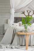 Leaves in glass vase on wooden bench at foot of double bed in pale bedroom