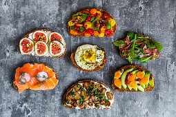Slices of bread topped with vegetables, Parma ham, mushrooms, salmon, figs and fried egg