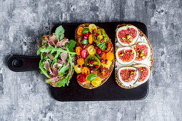 Slices of bread topped with figs, tomatoes, Parma ham and rocket