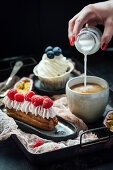 Eclair with berries and cream, and vanilla cupcake, pouring milk into coffee