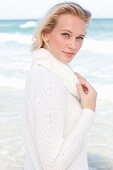 A young blonde woman by the sea wearing a white jumper