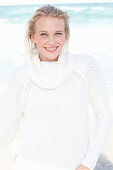 A young blonde woman by the sea wearing a white jumper