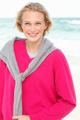 A young blonde woman wearing a pink jumper with a grey jumper over her shoulders