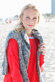 A young blonde woman wearing a red jumper with a grey jumper over her shoulders