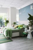 Bed line in shades of green on white double bed with headboard in open-plan bedroom
