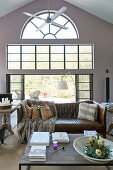 Coffee table, vintage leather sofa with fur blanket and cushions and candles on side table in front of terrace doors