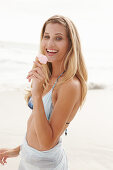 A blonde woman on a beach with an ice cream wearing a bikini